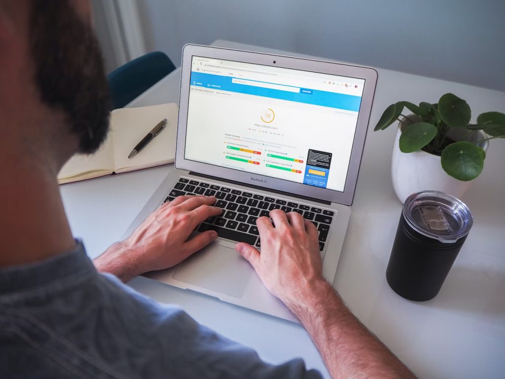 : A person's hands typing on a MacBook laptop, with a web browser showing a Google PageSpeed Insights report and a plant in the background.