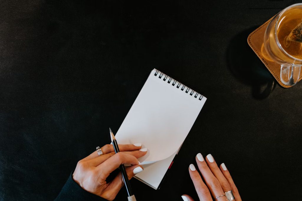 What is a Case Study: Overhead shot of hands holding a pencil over a blank spiral notebook on a dark surface, with a glass of tea in the top right corner, suggesting note-taking or planning.