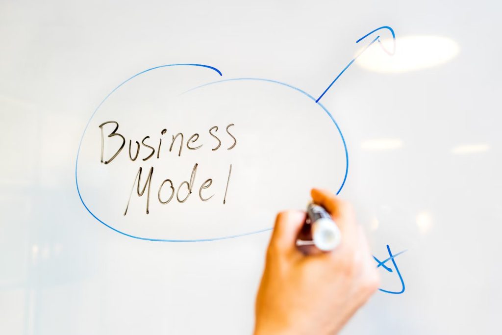 A hand drawing a blue circle around the words "Business Model" on a white board with an upward arrow, illustrating strategic planning.