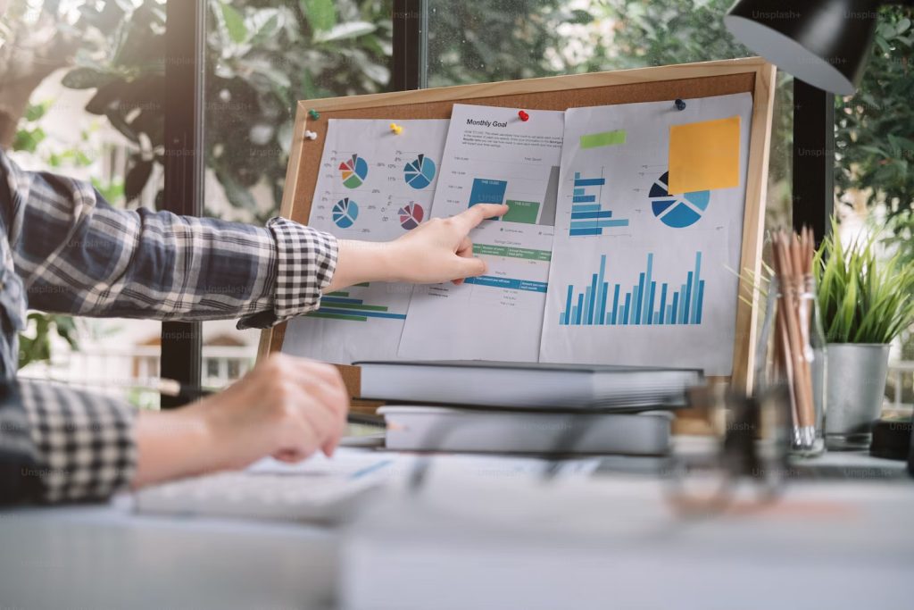 A hand points to pie charts and bar graphs on a corkboard, representing data analysis crucial for an effective SEO strategy.