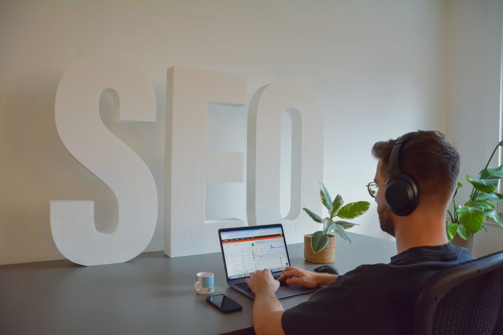 A person wearing headphones works on a laptop in front of large "SEO" letters, symbolizing dedicated SEO strategy implementation.