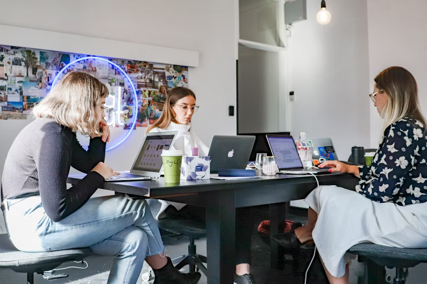 Three women collaborating on laptops in a modern office, planning social media marketing strategies.